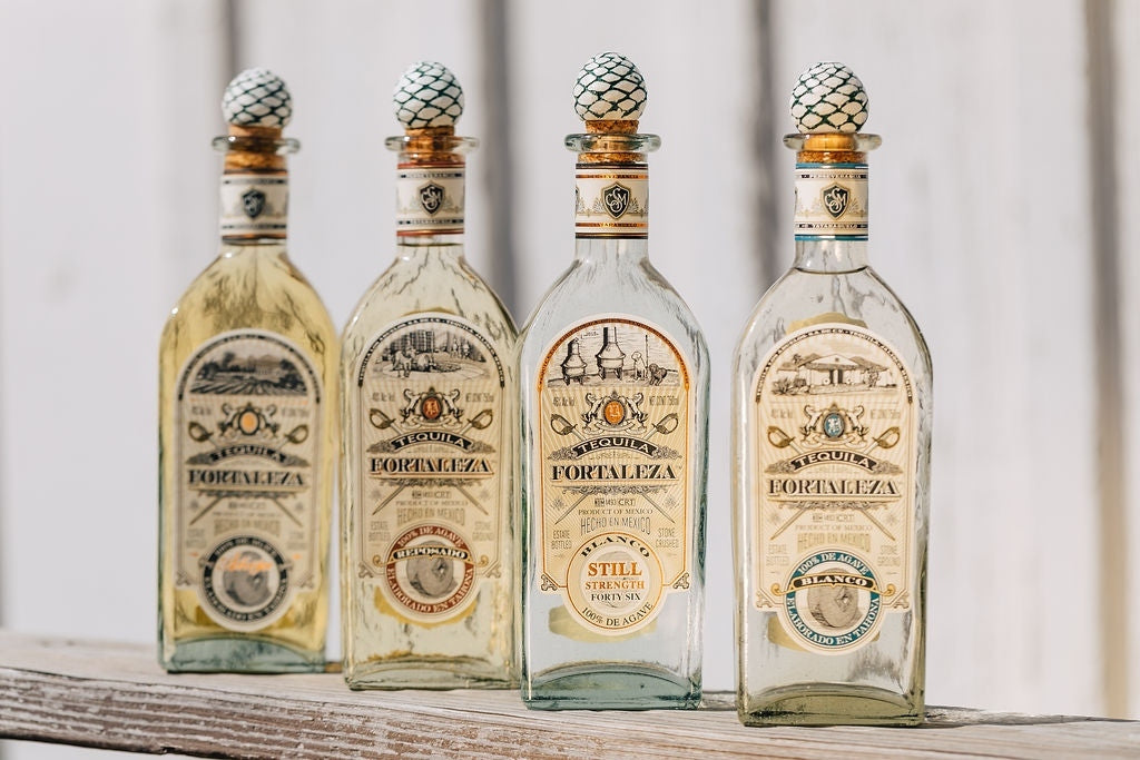 Four bottles of Fortaleza tequila on a wooden shelf
